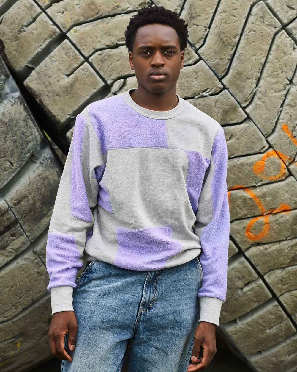 A boy wearing jeans and an upcycled crewneck sweater with heather grey and lavender pieces combined to make a unique geometric pattern.
