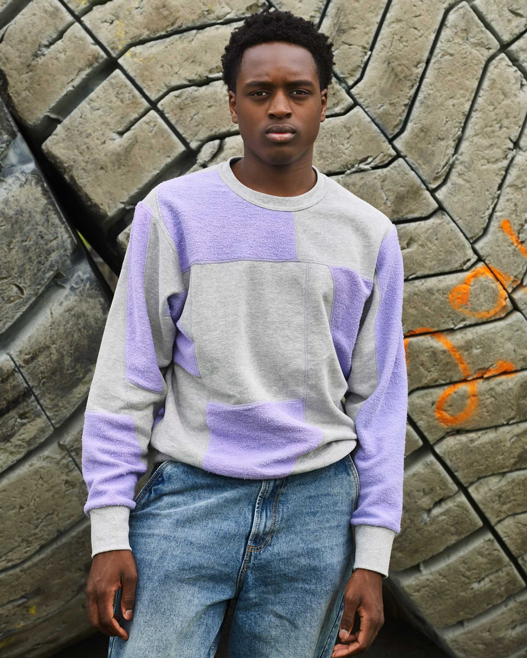 A boy wearing jeans and an upcycled crewneck sweater with heather grey and lavender pieces combined to make a unique geometric pattern.