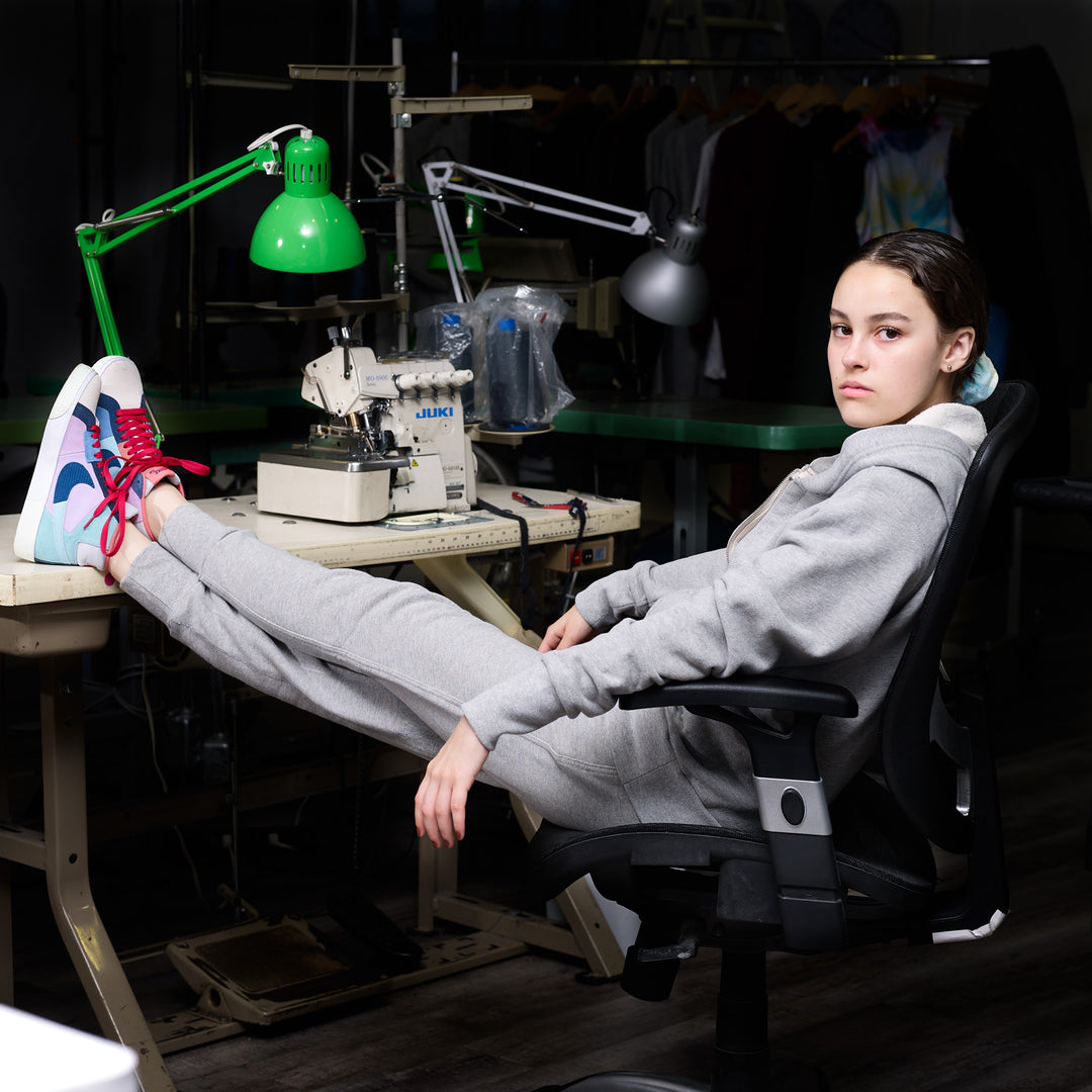 Model sitting at sewing machine in matching heather grey zip hoodie and sweatpants made in canada