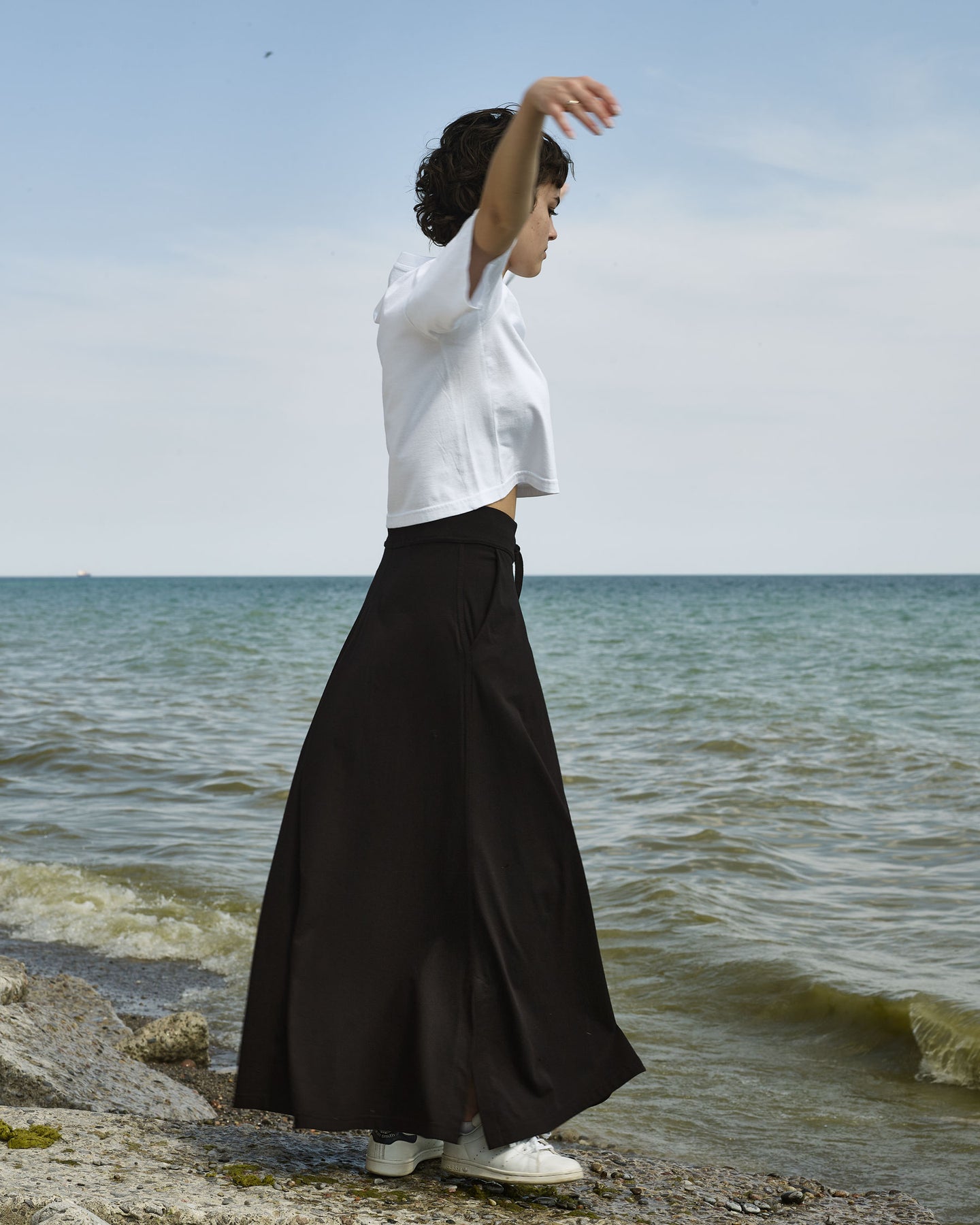 Girl twirling on beach in long black jersey skirt and white crop tee.
