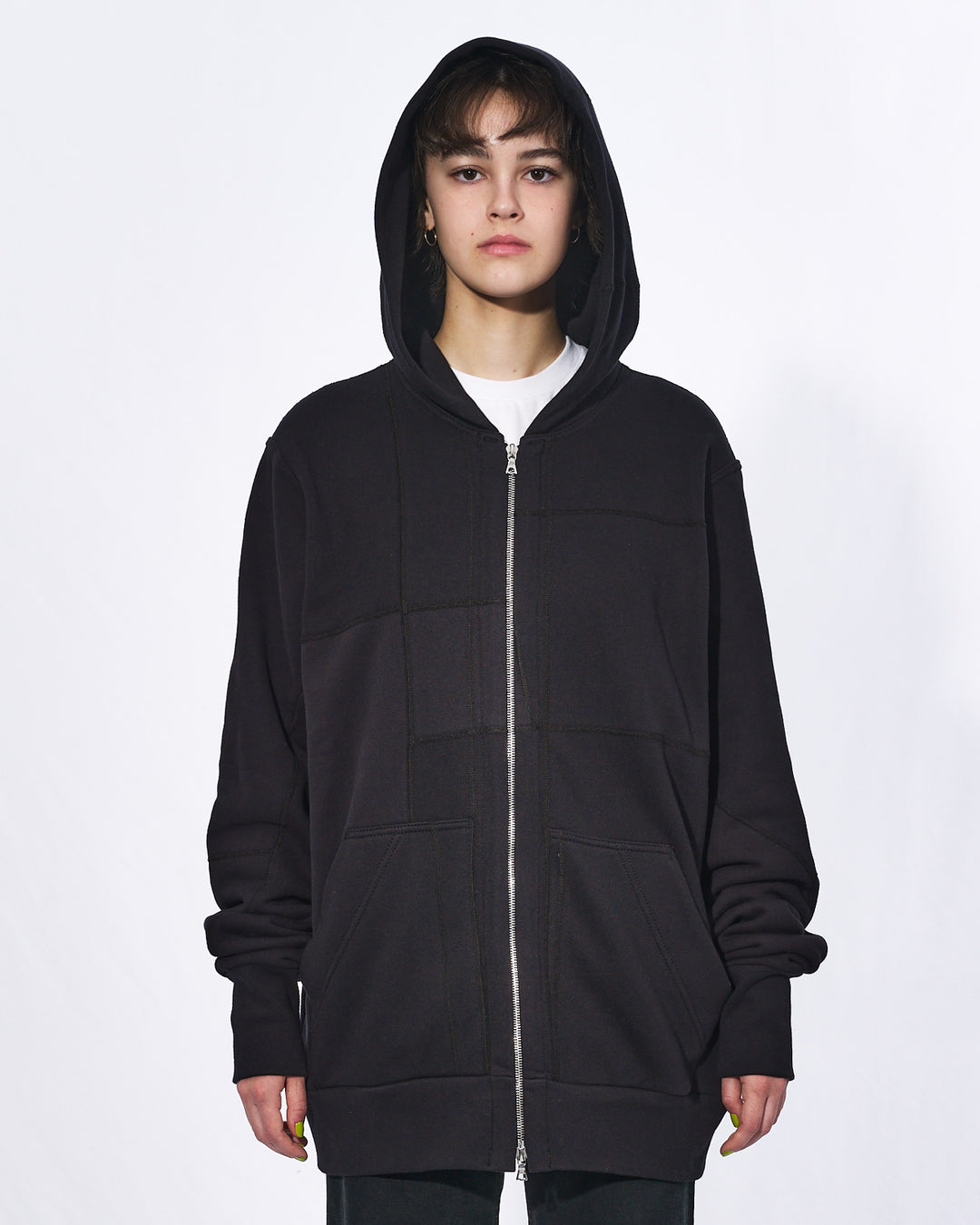 A girl with her hood up wearing an all black oversized upcycled hoodie with a silver two way zipper and two front pockets.