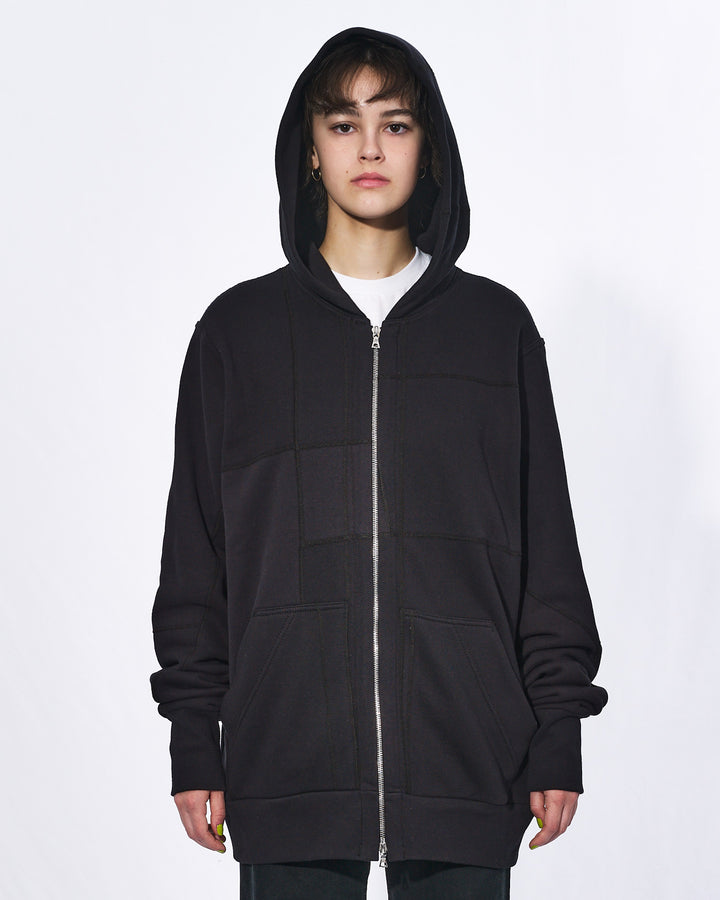 A girl with her hood up wearing an all black oversized upcycled hoodie with a silver two way zipper and two front pockets.