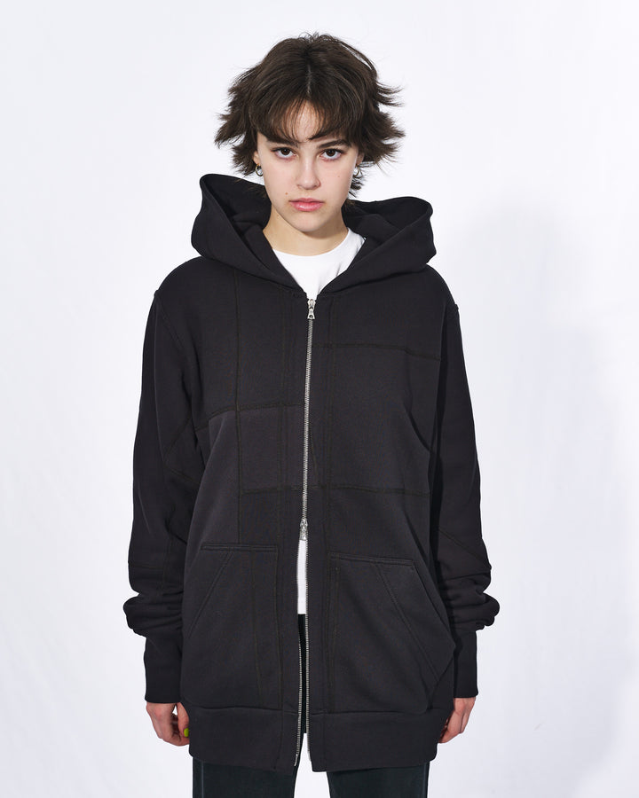 A girl with short black hair wearing an all black oversized upcycled hoodie with a silver two way zipper and two front pockets.