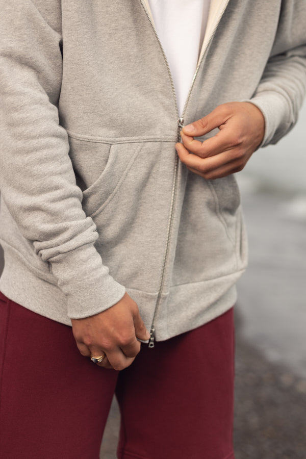 Hands zipping up a grey sweat shirt with a two way silver zipper and two front pockets.